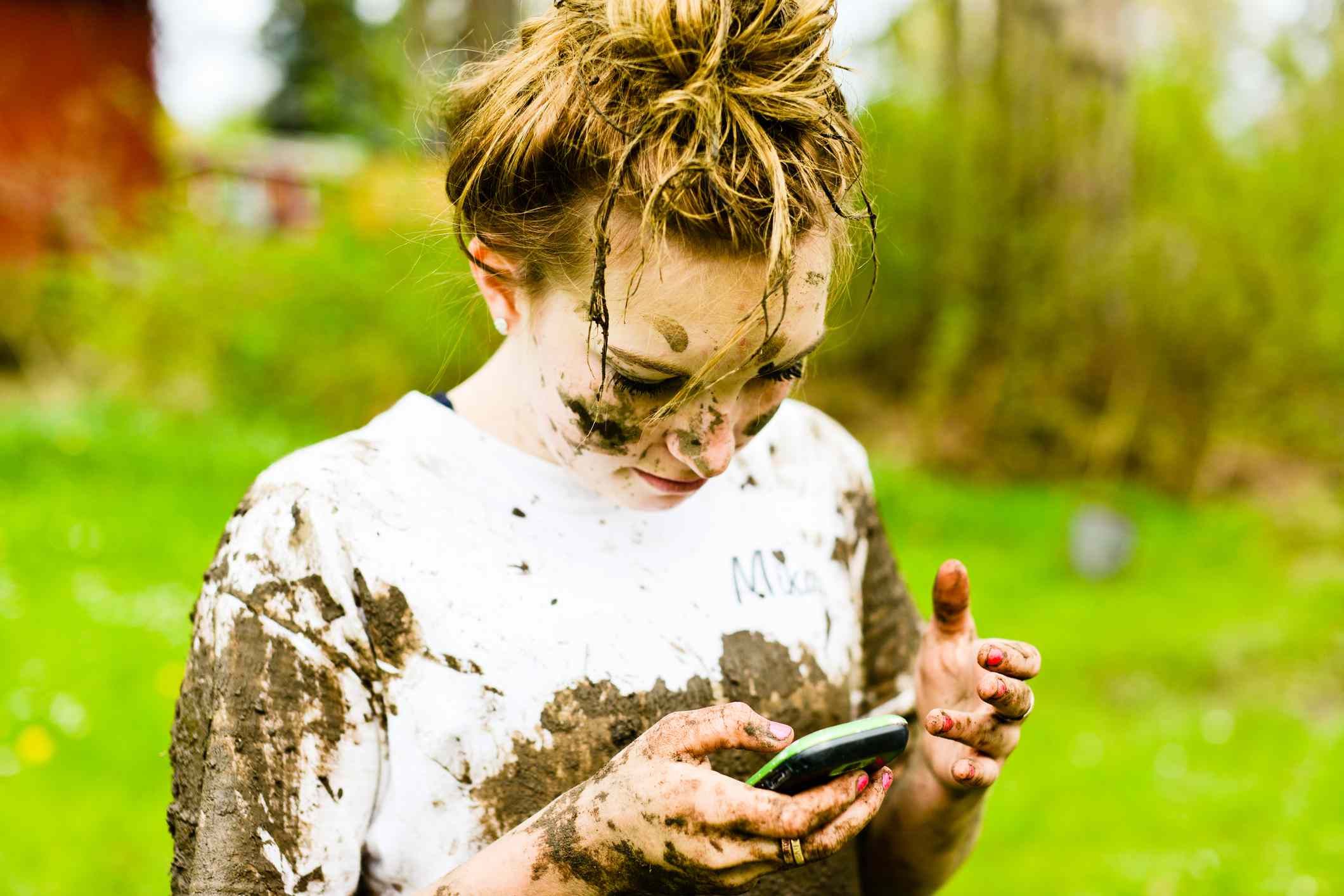 Изображение девушки с грязью на всем протяжении и телефона в руке.