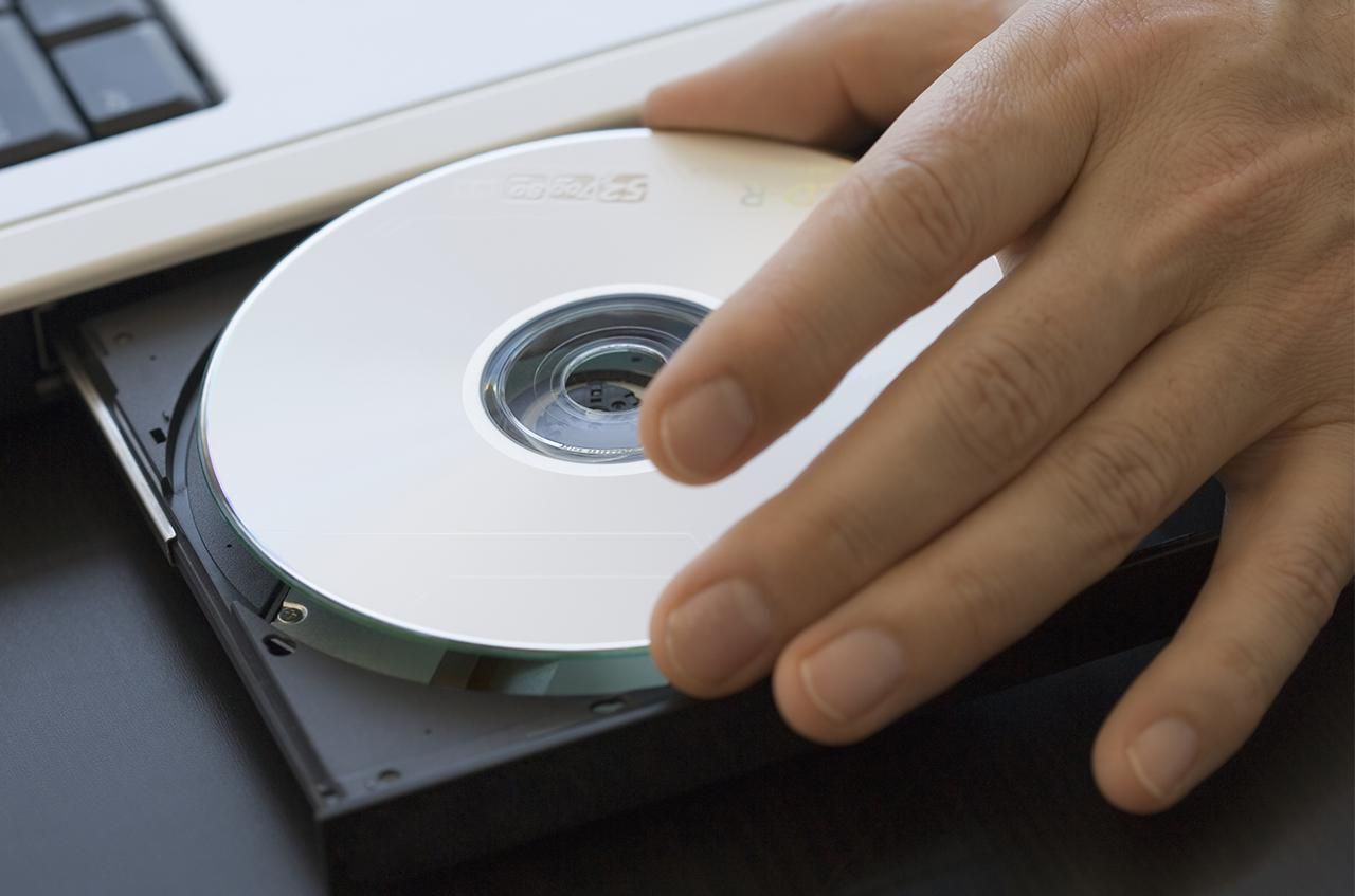 Зрелые положить компакт-диск в дисковод для ноутбуков, крупным планом руки.