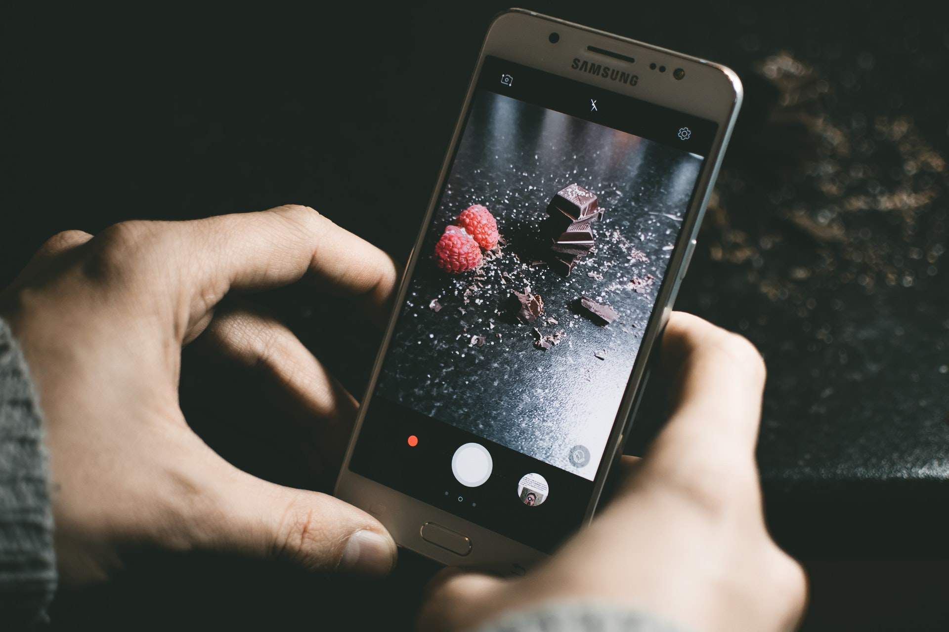 Человек фотографирует шоколад и клубнику с помощью смартфона