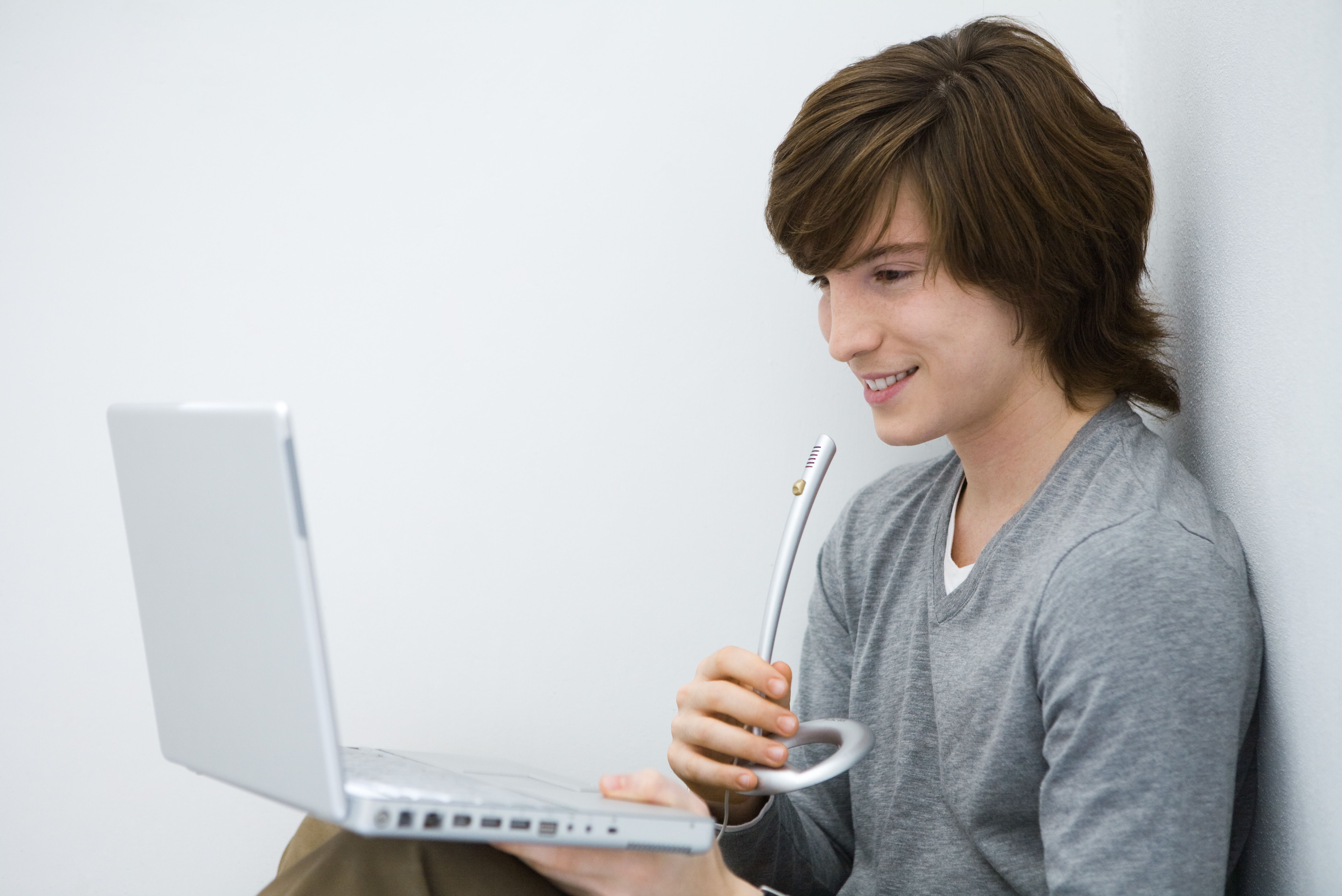 Молодой человек, глядя на портативный компьютер, выступая в микрофон, вид сбоку