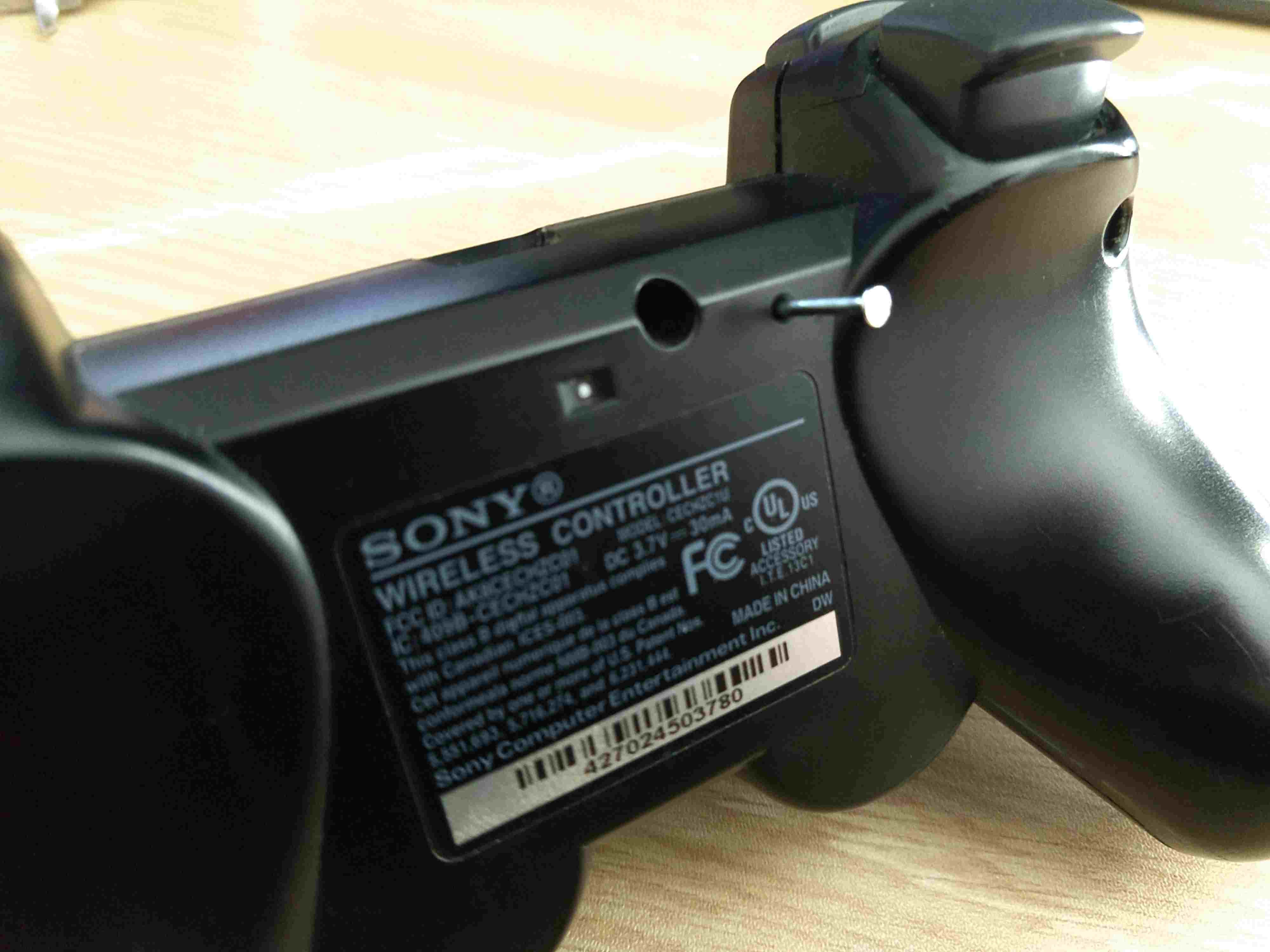 Инструмент, вставленный в отверстие для доступа к кнопке сброса на контроллере PS3.