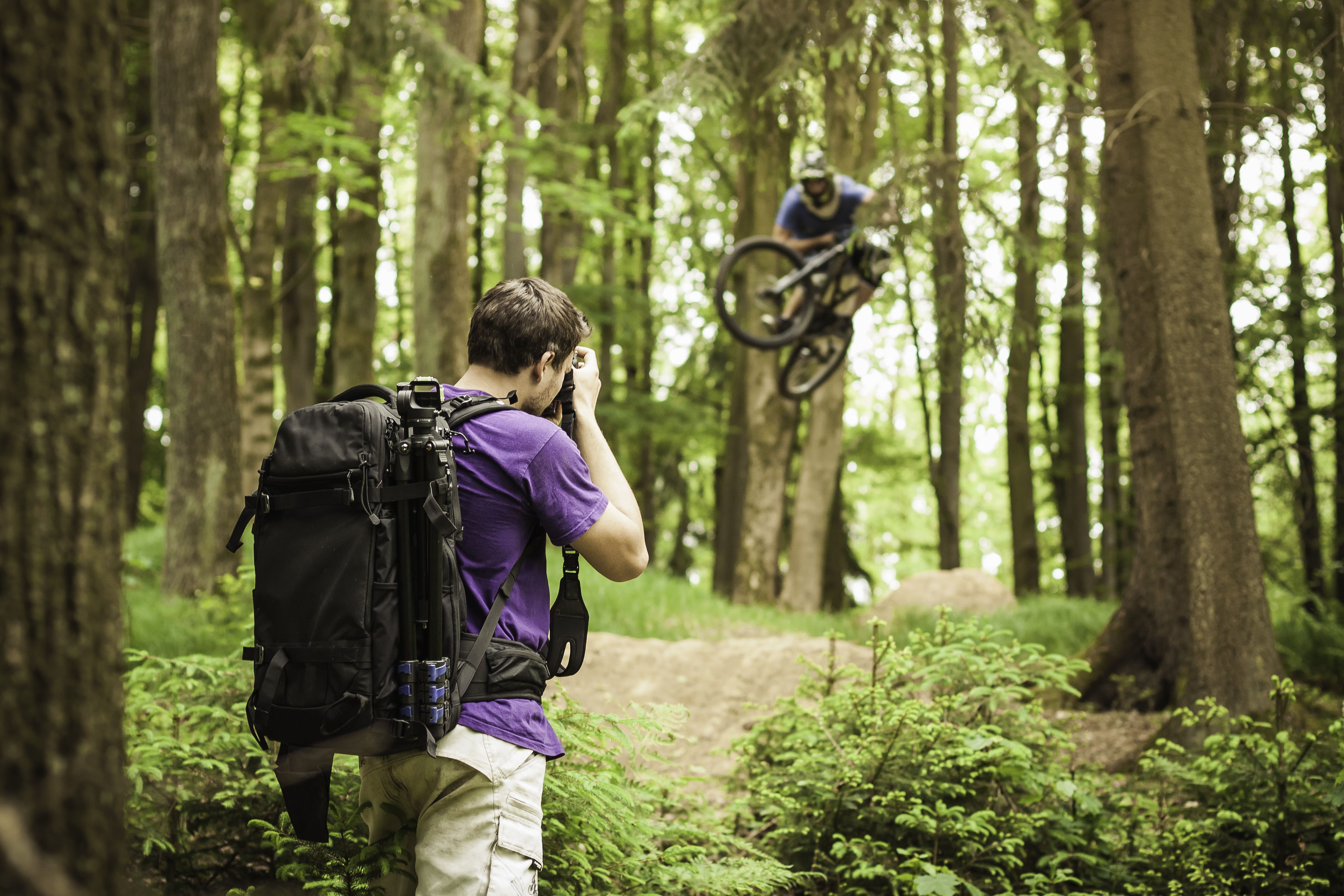 Молодой мужской фотограф фотографируя горного велосипедиста в лесе